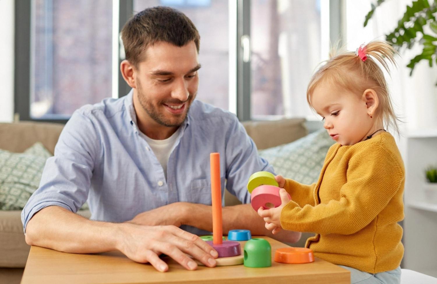 Father helping a toddler stack colourful rings on a wooden peg toy